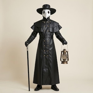 Könnte beinhalten: Ein Pestdoktor-Kostüm bestehend aus einem langen schwarzen Mantel mit Messingknöpfen, einem breitkrempigen Hut und einer weißen vogelartigen Maske. Das Outfit umfasst schwarze Handschuhe, schwarze Schuhe, einen schwarzen Gehstock und eine Metalllaterne.