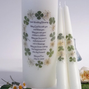 May include: A set of white candles, including a large pillar candle and two tapers. The pillar candle features an "Irish Wedding Blessing" with text and shamrock designs. The tapers also have shamrock accents. Daisies are at the base.