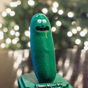 May include: A green, pickle-shaped figurine with a face, standing on a green base. The figurine has white eyes, a red mouth, and green drool. The base reads "I turned myself into a pickle, Morty!"