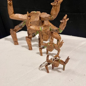 May include: A set of wooden sculptures depicting a character with raised arms. The brown figures have green detailing and vary in size, including a miniature keychain model.