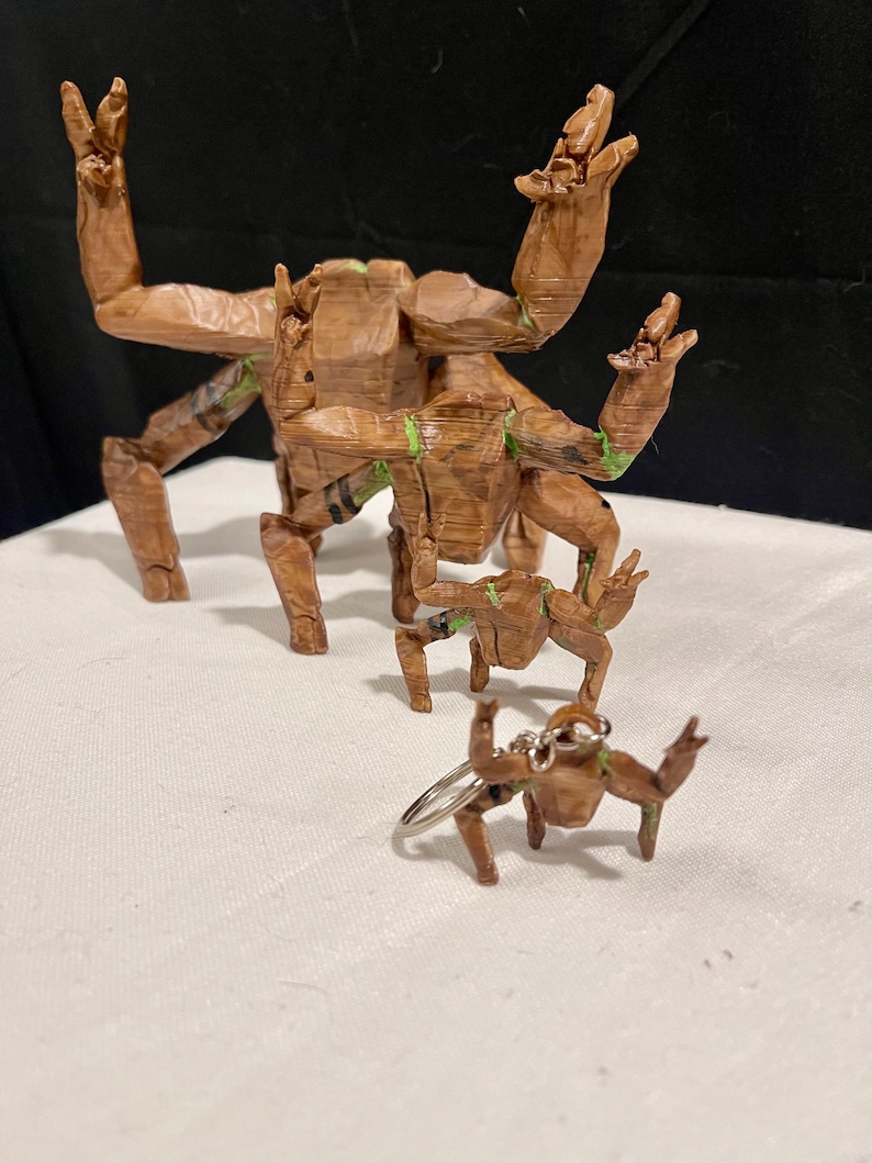 May include: A set of wooden sculptures depicting a character with raised arms. The brown figures have green detailing and vary in size, including a miniature keychain model.