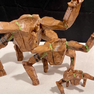 May include: Three wooden sculptures of a creature with outstretched arms and legs. The sculptures are brown with green accents and black stripes. The largest sculpture is in the centre, with two smaller ones on either side.