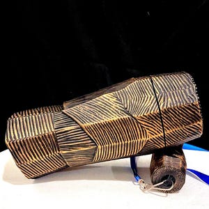 May include: A brown and gold decorative box with a textured, carved design. The box is rectangular with a cylindrical attachment and a blue ribbon. The box is on a white surface.