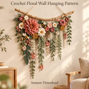 May include: A crochet floral wall hanging pattern featuring a large pink dahlia, white daisies, and small yellow flowers attached to a curved wooden branch. The design includes green crocheted leaves, hanging vines, and two small bumblebees.