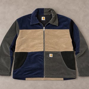 Könnte beinhalten: Eine farblich abgesetzte Cordjacke mit durchgehendem Frontreißverschluss, Umlegekragen und zwei Vordertaschen. Das Kleidungsstück besteht aus marineblauen, beigen, schwarzen und dunkelgrauen Stoffbahnen und trägt ein Carhartt-Label auf der Brust.