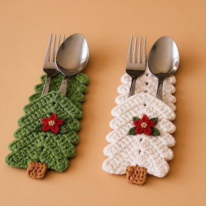May include: Two crochet utensil holders shaped like Christmas trees, one green and one white. Each holder features a small brown trunk, a red poinsettia flower with gold beads at the center, and contains a silver metal fork and spoon.