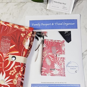 May include: A red fabric family passport and travel organizer with a white snap closure, featuring a botanical print of Australian flowers. The item is displayed alongside a printed instruction sheet titled Family Passport & Travel Organiser.