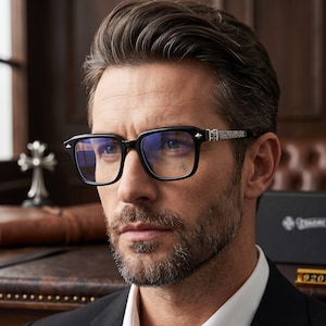 May include: Black rectangular eyeglasses featuring silver-toned metal temples with intricate engraved detailing and a small cross emblem on the lens. The frames have a polished finish and a sturdy bridge, providing a structured look.