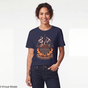 Può includere: Una t-shirt blu navy a maniche corte con una stampa grafica di un calderone nero sospeso sopra un falò. Il calderone contiene un liquido ribollente con vapore visibile, circondato da fiamme arancioni e gialle brillanti e pietre grigie.
