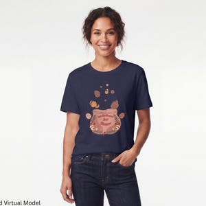 Può includere: Una t-shirt a maniche corte blu navy con la grafica di un calderone marrone chiaro da cui esce del vapore. Il calderone riporta la scritta Let the Season Just Simmer, circondata da piccole illustrazioni di foglie e ghiande.