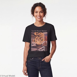 Può includere: Una t-shirt nera con una stampa grafica di un fornello da cucina con una pentola sul fuoco. Il vapore sale dalla pentola in motivi vorticosi. Sopra l'illustrazione, il testo recita "Let the Season Simmer" in un carattere semplice.