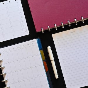 Puede incluir: Un cuaderno de discos magenta, un bolígrafo blanco y hojas de planificador sueltas. Una página muestra una cuadrícula de calendario mensual, mientras que otra presenta una lista de verificación con el texto FEBRUARY arriba. Hojas perforadas.