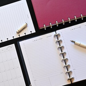 Puede incluir: Un sistema de agenda de discos con una cubierta magenta, una agenda abierta con páginas rayadas y una pluma estilográfica blanca, una hoja de calendario mensual separada, una hoja de tareas rayada con un bolígrafo blanco y pestañas de colores.