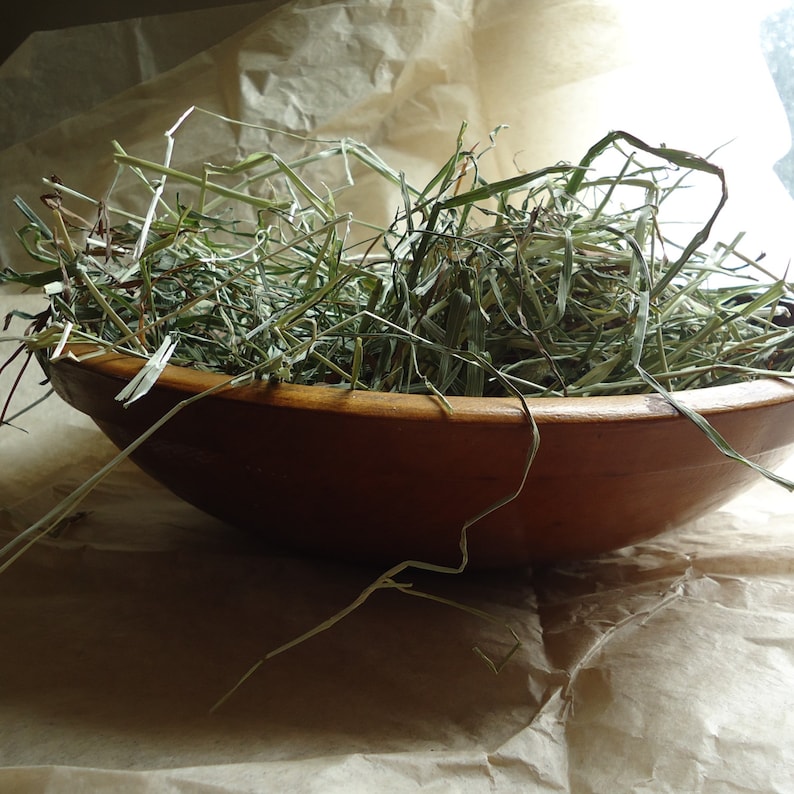 May include: A wooden bowl filled with dried green grass, sitting on a brown paper surface.