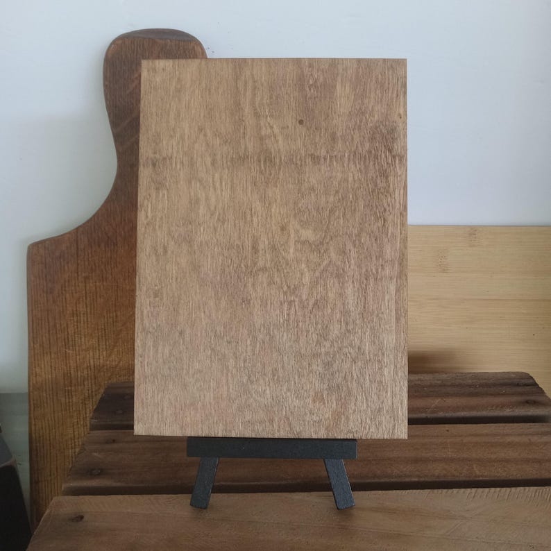 May include: A wooden sign with a natural wood finish, standing on a black easel. The sign is blank and ready to be customized.