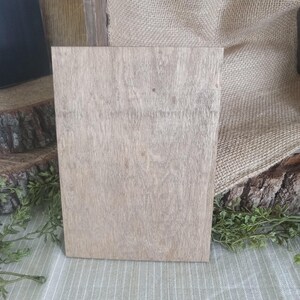 May include: A light brown wooden sign with a smooth, slightly textured surface. The sign is rectangular and has a natural wood grain pattern.