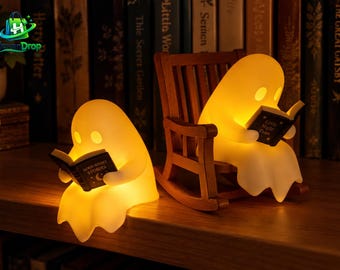 Puede incluir: Dos lámparas con forma de fantasma de tono cálido y brillante. Un fantasma está sentado sobre una superficie leyendo un libro titulado Good Night Stories. El otro está sentado en una pequeña mecedora de madera leyendo Little Night Tales.