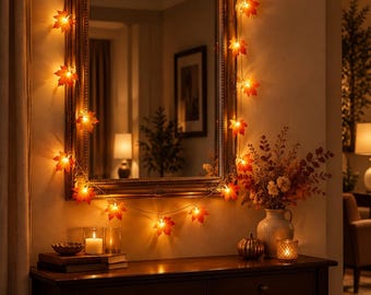 Puede incluir: Una guirnalda de luces LED con cubiertas de hojas de arce naranjas y rojas, dispuesta alrededor de un espejo rectangular con marco de madera oscura. Las luces emiten un brillo cálido que ilumina el espejo y la pared con tonos otoñales.