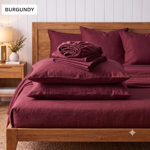 May include: A burgundy bedding set featuring a flat sheet, a fitted sheet, and two pillowcases arranged on a wooden bed frame. The fabric has a visible linen texture. The word BURGUNDY is printed in the upper left corner of the image.