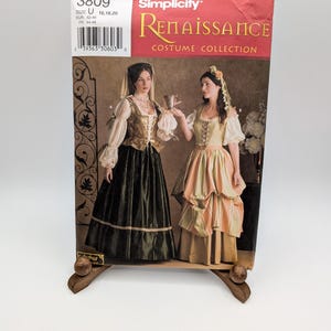 May include: A Simplicity Renaissance Costume Collection sewing pattern envelope, number 3809, size U 16, 18, 20. The front features two illustrations of historical-style dresses with long sleeves, bodices, and full skirts, along with a barcode.