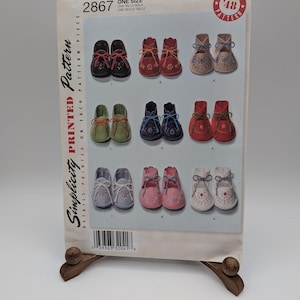 May include: A Simplicity 2867 sewing pattern envelope for baby moccasins in one size. The front displays nine pairs of shoes in various colors including black, red, tan, green, blue, pink, and white, each featuring decorative stitching and laces.