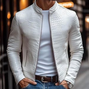 May include: A white jacket with a textured crocodile skin pattern, featuring a stand-up collar, a full-length front zipper, and long sleeves. The jacket is worn over a plain white t-shirt, paired with blue denim jeans and a brown leather belt.