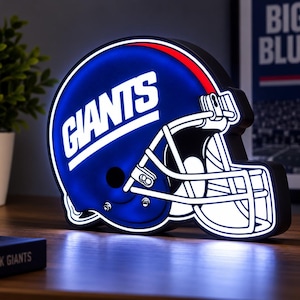 May include: A blue and white LED light shaped like a football helmet with the word GIANTS printed in white across the side. The helmet features a white face mask and a red stripe along the top edge, emitting a bright blue glow from the interior.