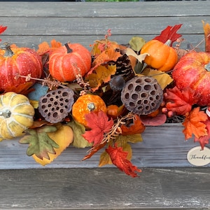 May include: A wooden box centerpiece decorated with fall foliage, pumpkins, gourds, and dried lotus pods. The box has a sign that reads "Thankful".