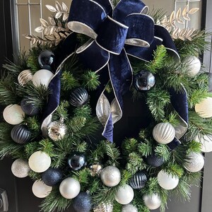 May include: A Christmas wreath decorated with a navy blue velvet bow and silver and blue ornaments.