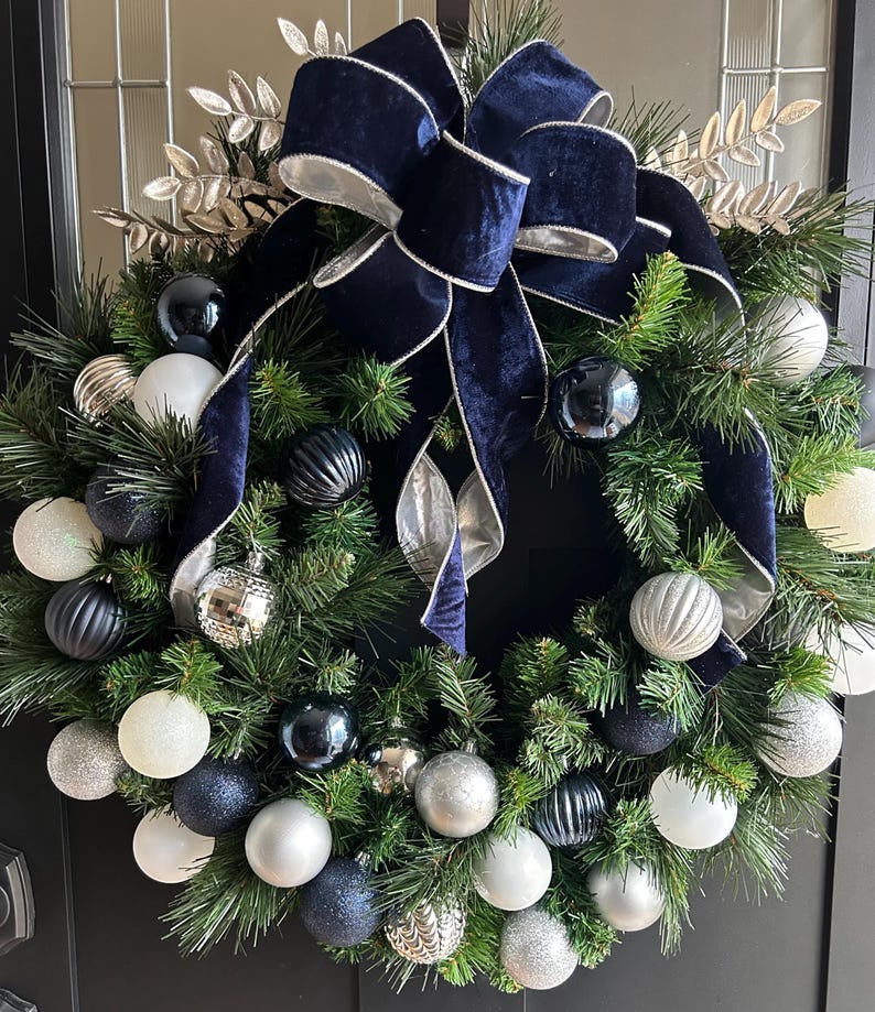 May include: A Christmas wreath decorated with a navy blue velvet bow and silver and blue ornaments.