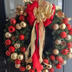 May include: A Christmas wreath with red and gold ornaments, pine branches, and a large red and gold bow.
