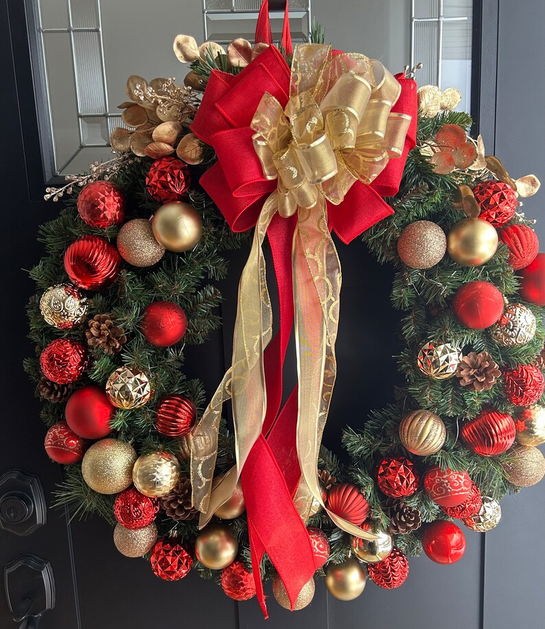 May include: A Christmas wreath with red and gold ornaments, pine branches, and a large red and gold bow.