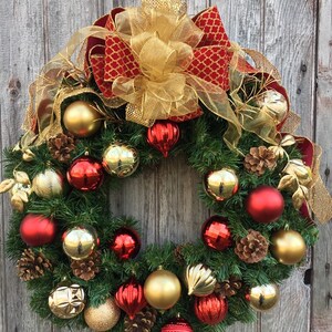 May include: A Christmas wreath decorated with red and gold ornaments, pine cones, and a large gold and red bow.