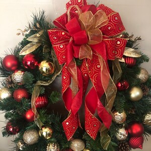 May include: A Christmas wreath decorated with red and gold ornaments, pine branches, and a large red bow with gold accents.