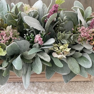 May include: A wooden box centerpiece filled with a variety of greenery, including lambs ear and pink flowers.