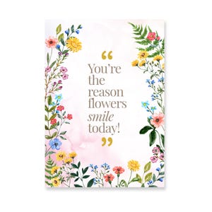 Può includere: Un biglietto d'auguri rettangolare con un bordo di fiori selvatici ad acquerello gialli, rosa e blu e felci verdi. Al centro è presente il testo "You're the reason flowers smile today!" in un carattere serif grigio scuro con virgolette dorate.