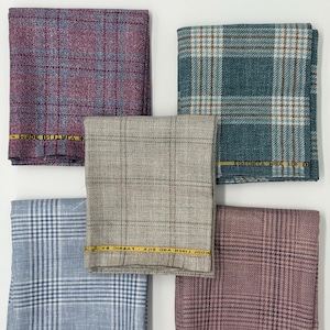 Könnte beinhalten: Fünf gefaltete Stoffquadrate mit Karomuster in Lila, Petrol, Hellgrau, Hellblau und Mauve. Jedes Stück hat eine gelbe Webkante mit dem in Schwarz gedruckten Text MADE FOR FABRIC. Die Textilien zeigen ein gewebtes Gittermuster.