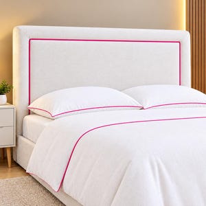 May include: A light beige upholstered headboard featuring a vibrant hot pink piped border. The bed is dressed in white bedding, including two pillows and a duvet cover, each accented with a matching hot pink piped trim along the edges.
