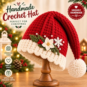 Könnte beinhalten: Eine rote Häkelmütze mit weißem Rippsaum und einem weißen Bommel an der Spitze. Die Mütze ist mit einem weißen Weihnachtsstern, grünen Blättern, roten Beeren, einer weißen Schneeflocke und kleinen weißen Perlen verziert. Text Handmade Crochet Hat.