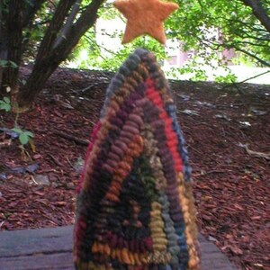 May include: A colorful, hand-stitched wool rug in the shape of a Christmas tree with a star on top. The rug is made of various shades of brown, red, blue, and green wool.