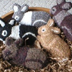 Könnte beinhalten: Fünf handgefertigte Filzkaninchen in einer Holzschale. Die Kaninchen sind in verschiedenen Farben, darunter Braun, Schwarz, Weiß und Grau.