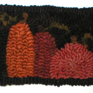 May include: A close-up of a hand-stitched rug with three pumpkins in shades of orange and red. The pumpkins are surrounded by a black background.