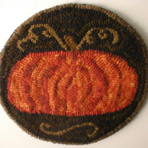 May include: A round, orange pumpkin rug with a brown and black border. The border has a swirling design.
