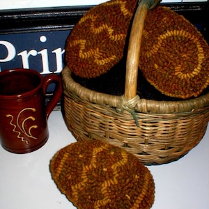 May include: Three brown and gold needlepoint wool circles in a wicker basket. The circles have a geometric pattern. The basket has a wooden handle.