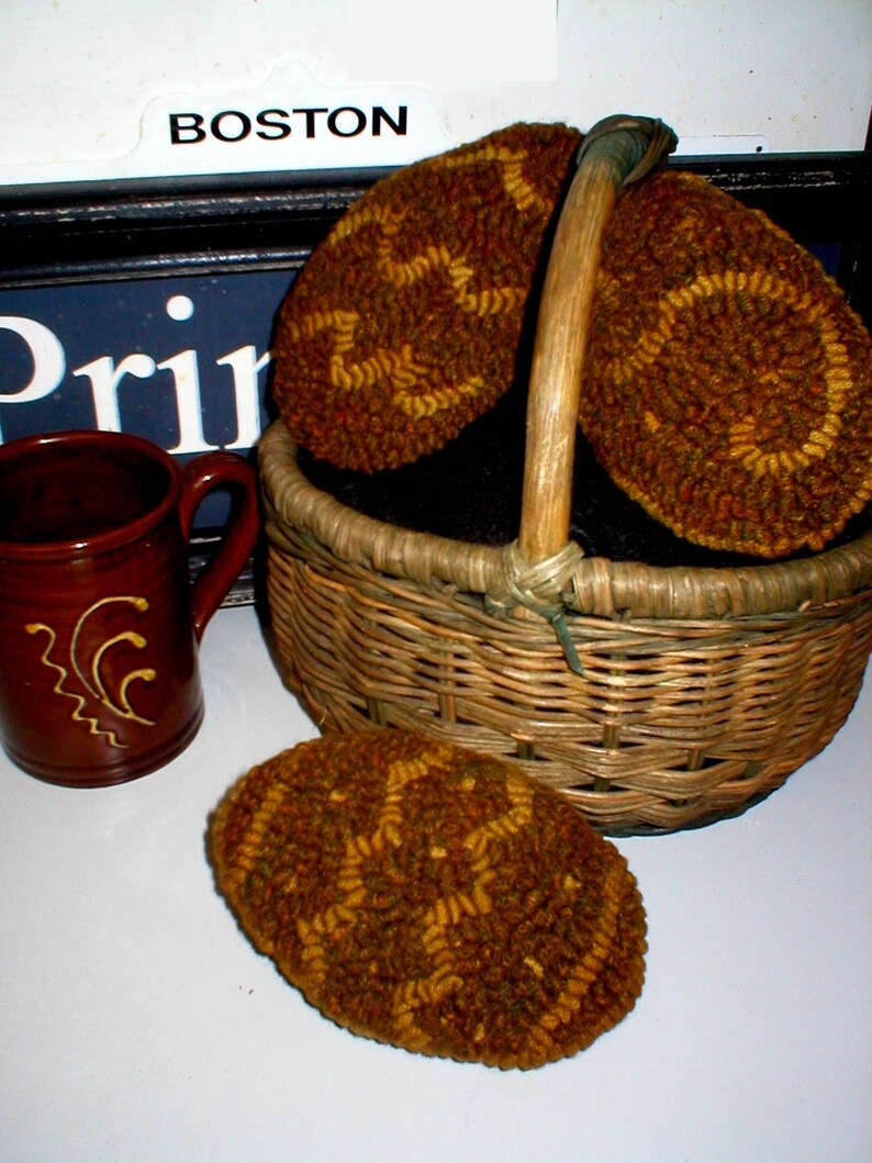 May include: Three brown and gold needlepoint wool circles in a wicker basket. The circles have a geometric pattern. The basket has a wooden handle.
