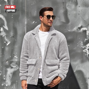 May include: A light gray, long-sleeved, button-down jacket made of a fuzzy, textured fleece material. The jacket features a notched lapel collar and two large, rectangular patch pockets on the front, worn over a plain white t-shirt.