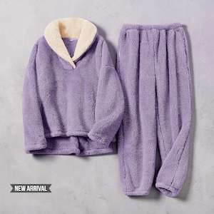 Könnte beinhalten: Ein zweiteiliges Lounge-Set aus flauschigem, violettem Fleece-Material. Das Oberteil hat einen breiten, cremefarbenen Schalkragen und lange Ärmel. Die passende Hose hat einen elastischen Bund und eine lockere Passform. Text NEW ARRIVAL.