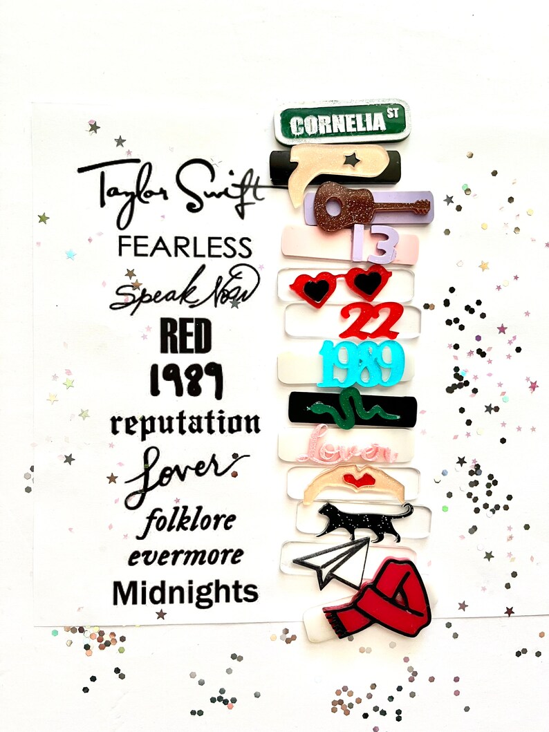 May include: A white card with the text "Taylor Swift" and the names of her albums: "Fearless", "Speak Now", "Red", "1989", "reputation", "Lover", "folklore", "evermore", and "Midnights".  The card is decorated with colorful stickers representing each album.