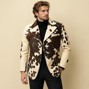 May include: A blazer featuring a brown and white cow print pattern with a notched lapel, two front buttons, and two flap pockets. The garment is worn over a black turtleneck sweater and paired with black trousers, creating a structured look.
