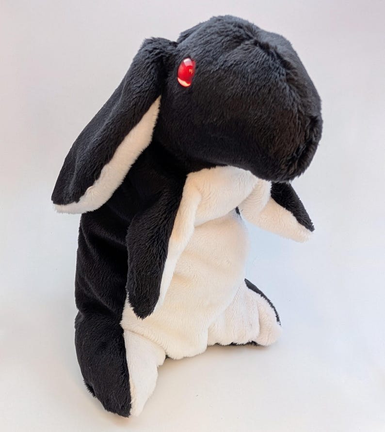 May include: A plush toy rabbit in black and white, with long ears and red eyes. The stuffed animal has a soft, fluffy texture and is designed to resemble a rabbit. The toy is suitable for children and makes a great gift.